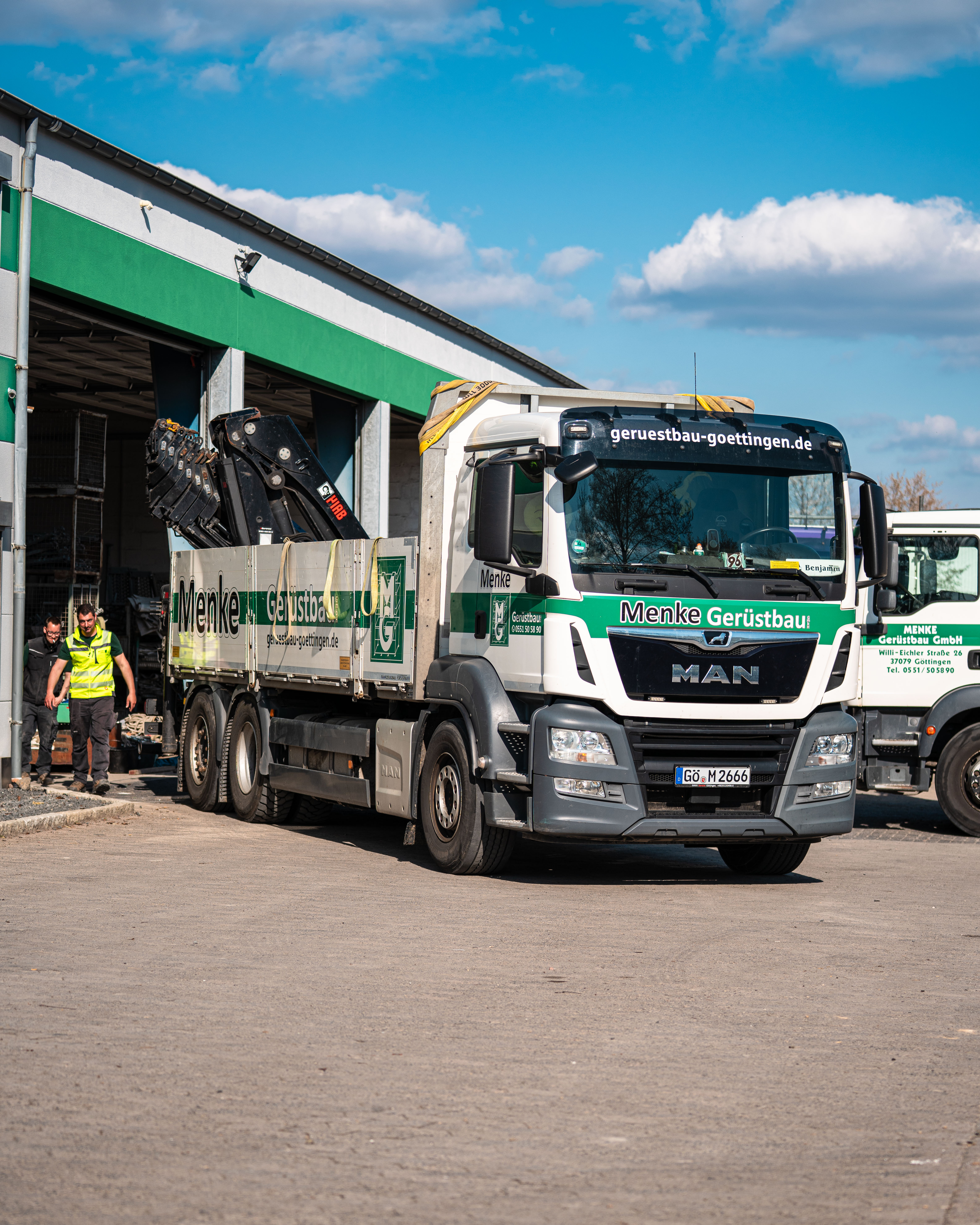 Menke-MAN-LKW mit Ladekran und Materialpritsche auf dem Betriebshof in Göttingen, im Hintergrund zwei Mitarbeiter an der Halle